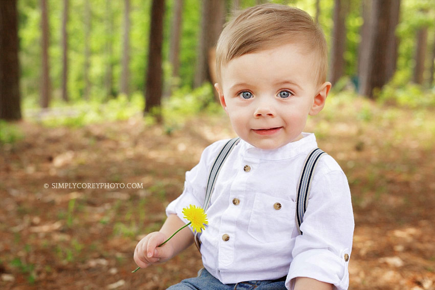 baby photographer Carrollton, GA, boy in suspenders holding a dandelion