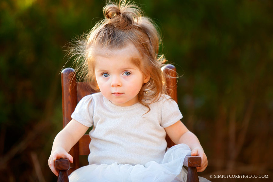 Villa Rica baby photographer, toddler with a top knot outside in a chair