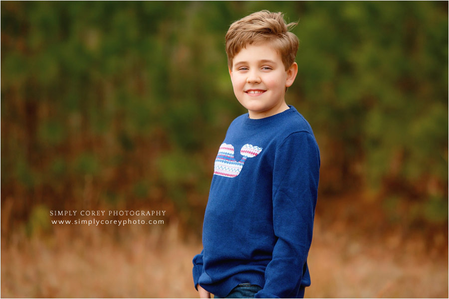 Villa Rica children's photographer, child in blue sweater outside by pines