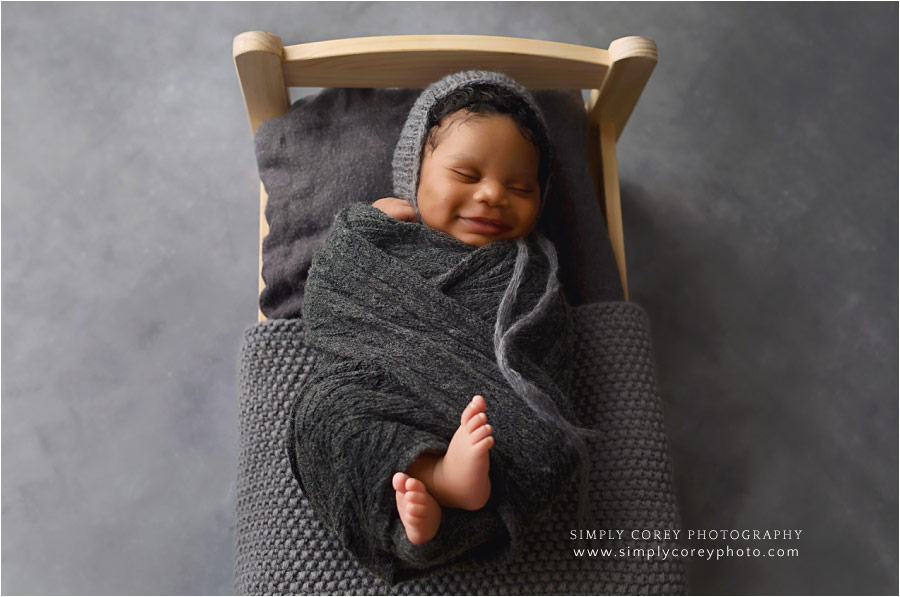 Carrollton newborn photographer, baby boy smiling on little bed