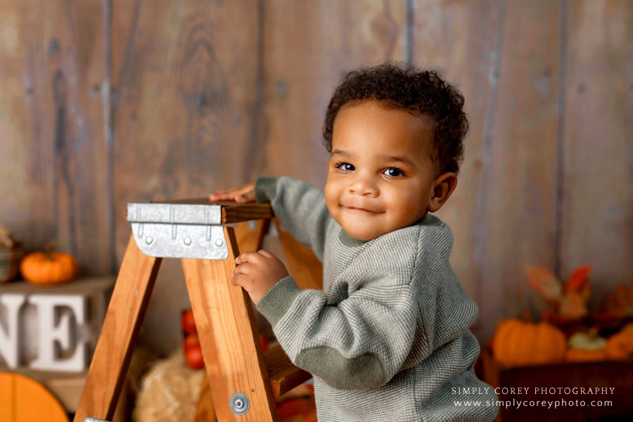 Atlanta baby photographer, one year old boy smiling with ladder during fall studio session