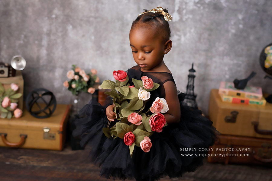 Newnan baby photographer, 2 year old in black dress looking at flowers
