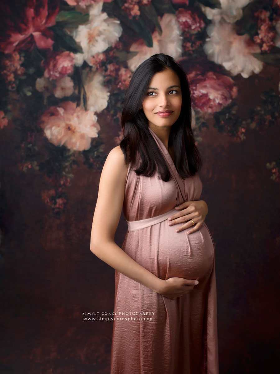 maternity photographer near Carrollton, GA; mom in pink dress with floral backdrop
