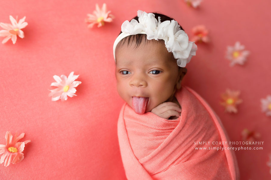 newborn photographer near Newnan, baby girl sticking tongue out on coral studio backdrop