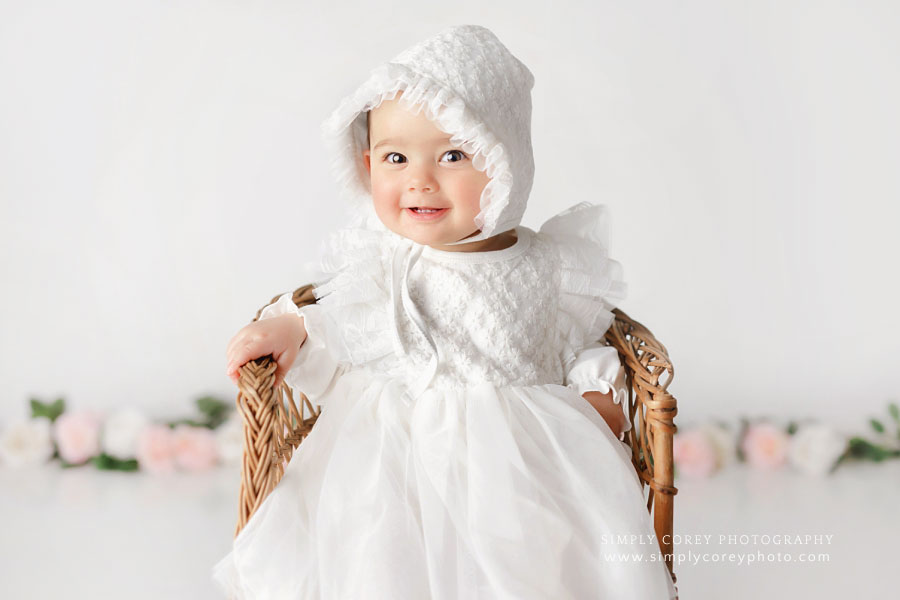 Carrollton baby photographer in GA; girl in white dress with wicker chair and flowers