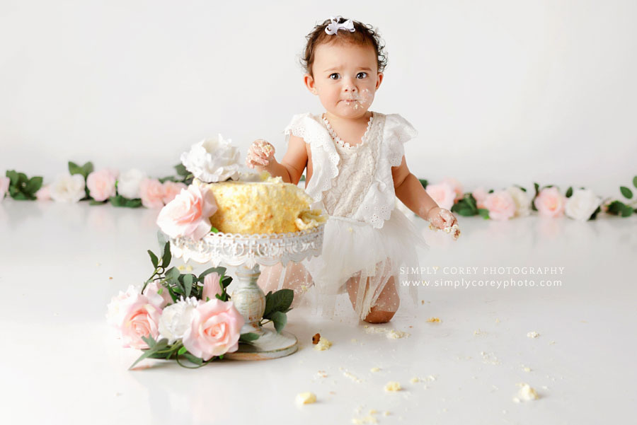 Carrollton cake smash photographer in Georgia, baby eating cake on white set with flowers
