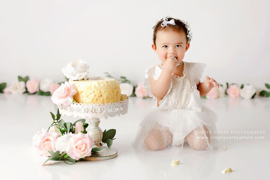Newnan cake smash photographer, baby girl eating cake on white set with flowers