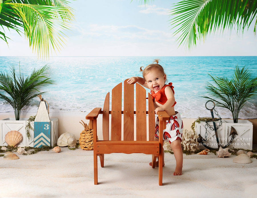 baby photographer near Peachtree City, girl laughing during studio beach session with adirondack chair
