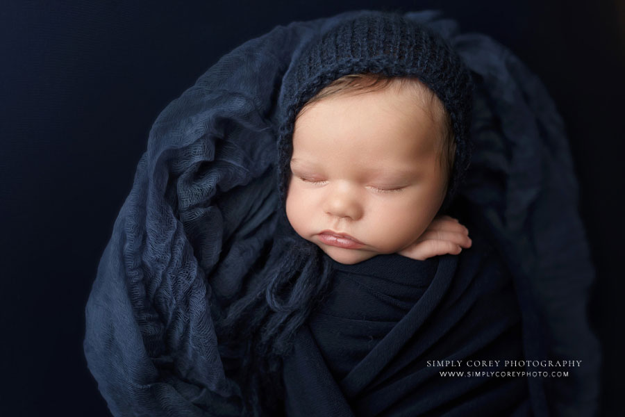 newborn photographer near Villa Rica, baby boy with navy blue hat, wrap, and studio backdrop