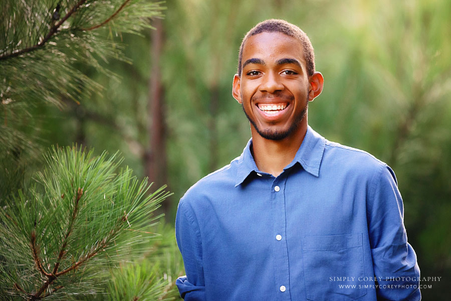 senior portrait photographer near Newnan, teen boy smiling outside by pine tree