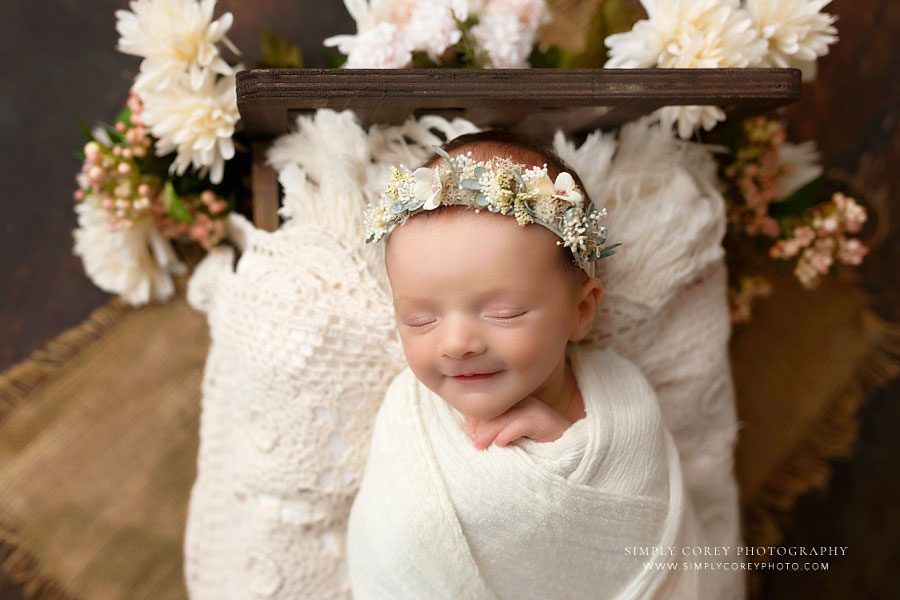 Atlanta newborn photography session, baby girl smiling on little bed with flowers