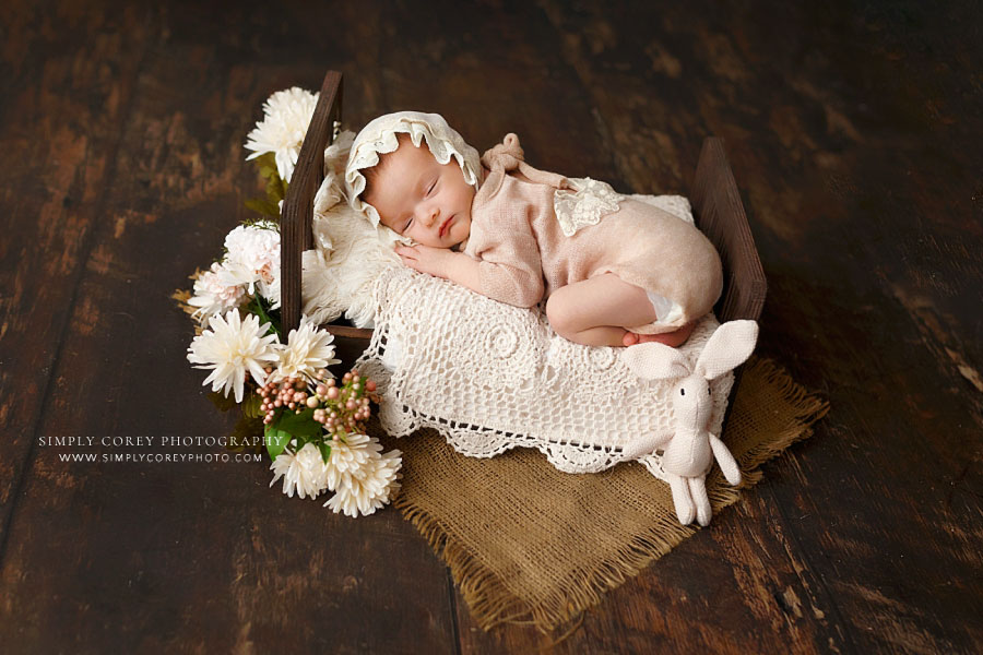 newborn photographer near Mableton, baby girl on small brown bed in studio with flowers