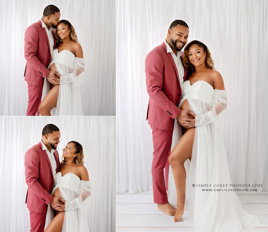 maternity photographer near Douglasville, mom with dad in pink suit in studio by white curtains